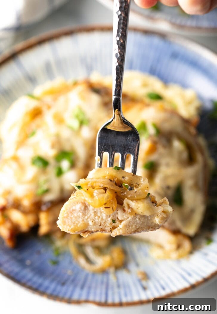 Plate of mashed potatoes topped with French onion chicken breast and gravy. A fork is holding a bite to camera.