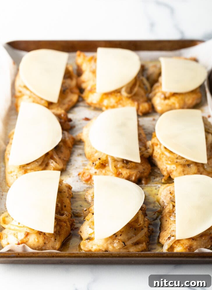 9 chicken thighs on a baking sheet topped with unmelted provolone cheese.