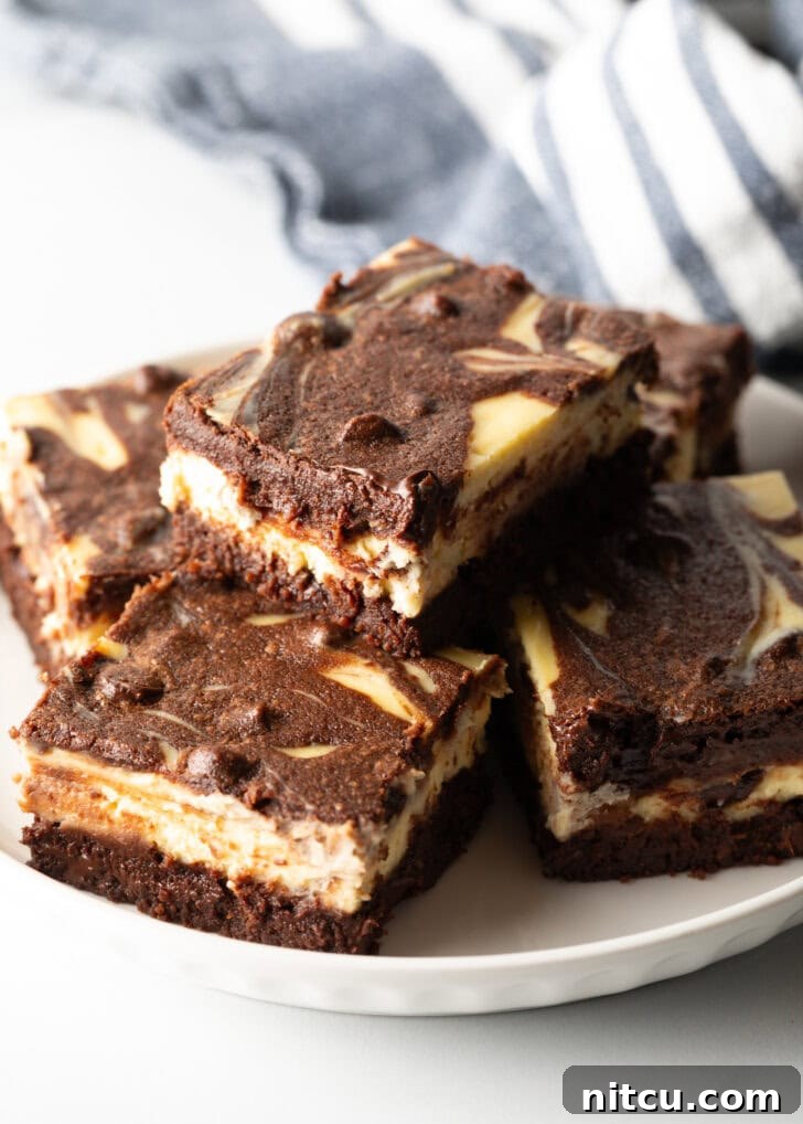 Decadent Brownie Cheesecake Bars 2 A plate featuring five delicious cheesecake brownies, with one stacked invitingly on top of another.