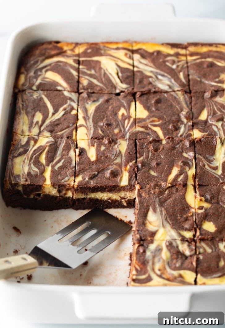 Decadent Brownie Cheesecake Bars 14 A pan of delicious brownies, with a few pieces already taken, and a metal spatula resting gently in the pan, ready for serving.