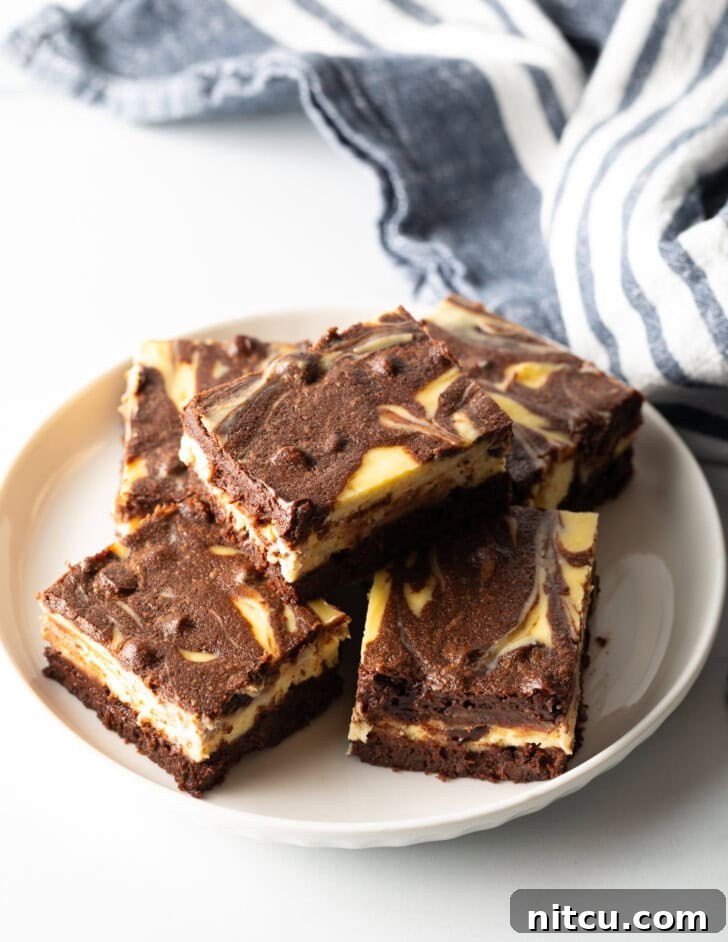 Decadent Brownie Cheesecake Bars 15 A top-down view of a plate featuring five irresistible cheesecake brownies, with one beautifully stacked on top, showing off its perfect layers.