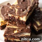 Decadent Brownie Cheesecake Bars 17 A plate features five delicious cheesecake brownies, with one stacked invitingly on top, highlighting the rich swirl.