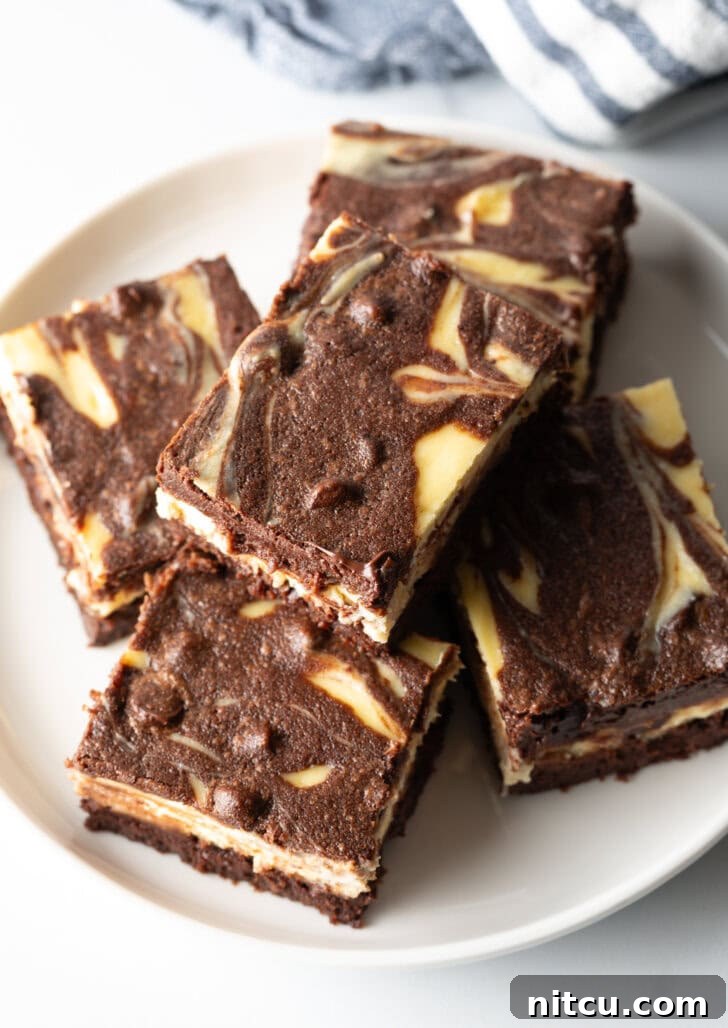 Decadent Brownie Cheesecake Bars 3 A top-down view of a plate showcasing five decadent cheesecake brownies, with one delicately stacked atop another, highlighting the rich swirl.