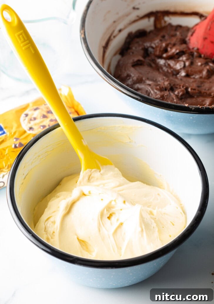 Decadent Brownie Cheesecake Bars 8 A yellow spatula is stirring a smooth, creamy cream cheese filling in a small white bowl, ready for layering.