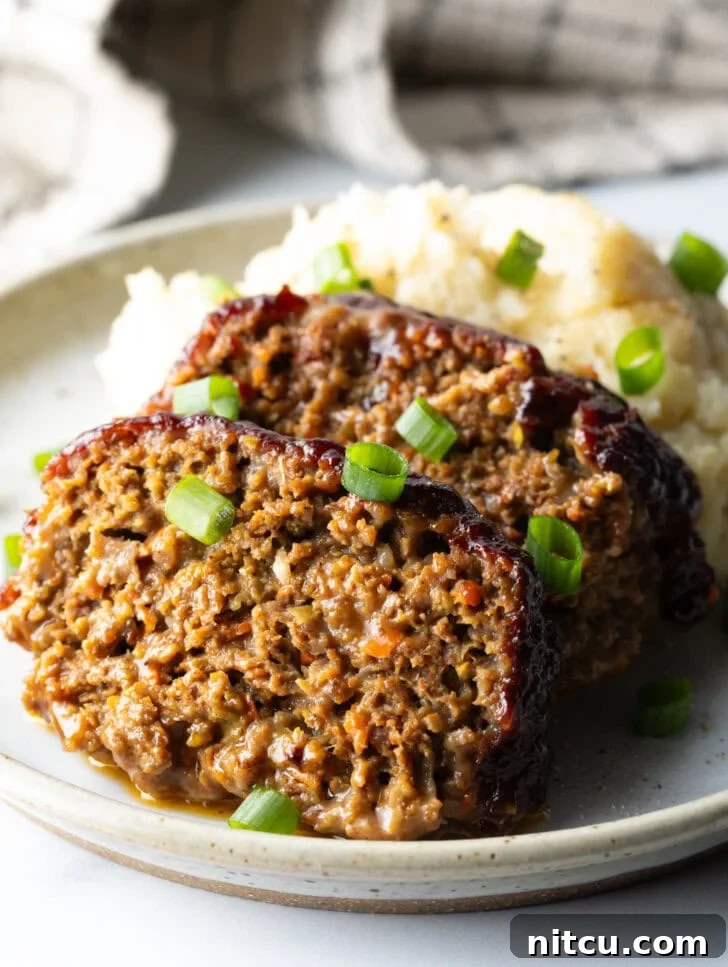 Pitmaster's Meatloaf 2 Two generous slices of smoked meatloaf, perfectly browned and glazed, served on a plate alongside a creamy scoop of mashed potatoes, all elegantly garnished with fresh chopped green onions.