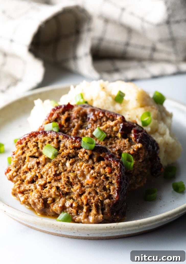 Pitmaster's Meatloaf 12 Two slices of smoked meatloaf resting on a plate, accompanied by a generous serving of mashed potatoes, and garnished with vibrant chopped green onions for a fresh finish.