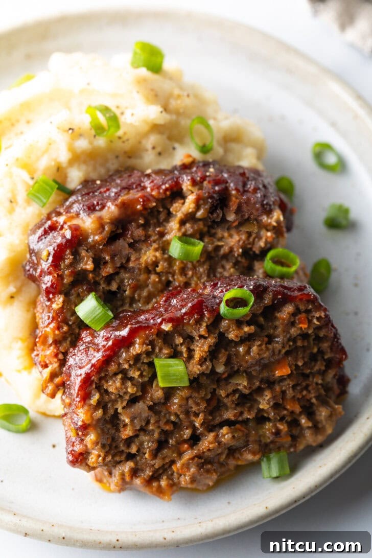 Pitmaster's Meatloaf 13 Two slices of tender, moist smoked meatloaf, artfully placed on a plate with a dollop of creamy mashed potatoes and a sprinkle of fresh green onions, ready to be enjoyed.