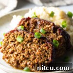 Pitmaster's Meatloaf 14 Two slices of meatloaf on a plate with a scoop of mashed potatoes, all topped with chopped green onions for garnish.