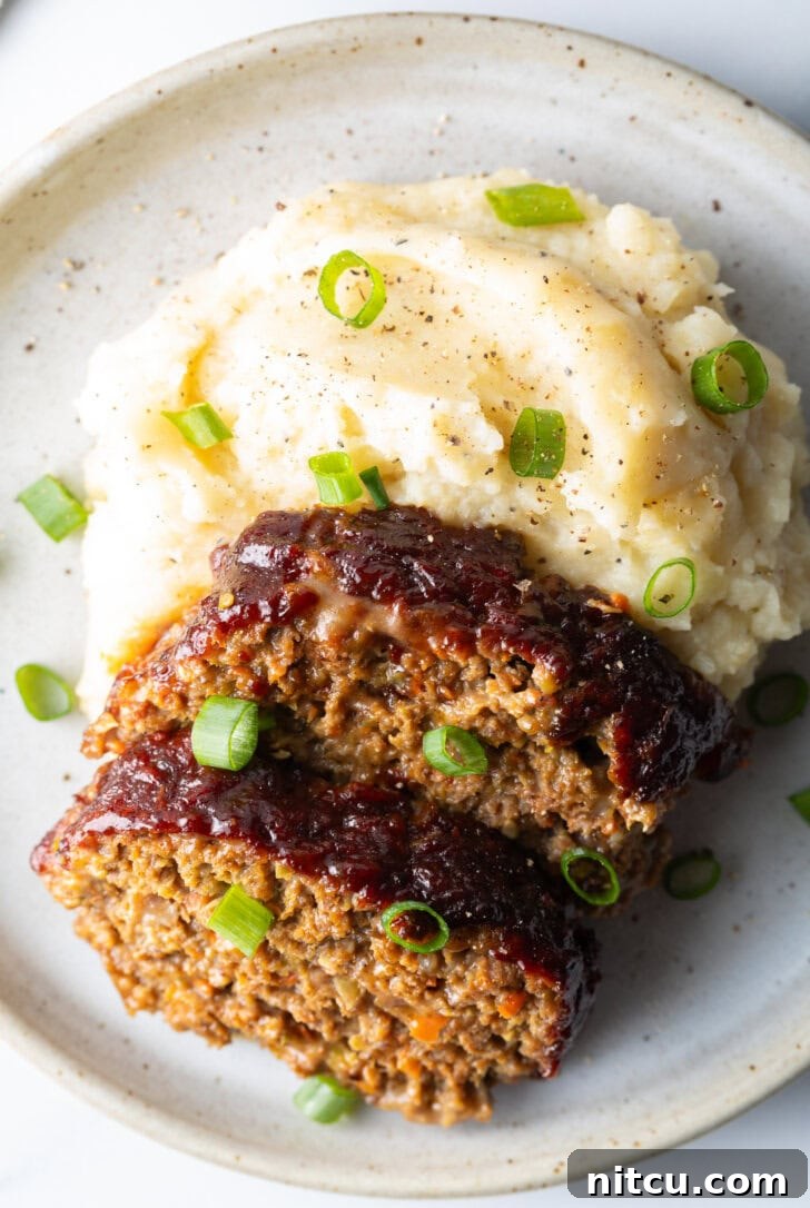 Pitmaster's Meatloaf 3 Two beautiful slices of smoked meatloaf arranged on a plate next to a fluffy portion of mashed potatoes, with a sprinkle of fresh green onions adding a pop of color and freshness.