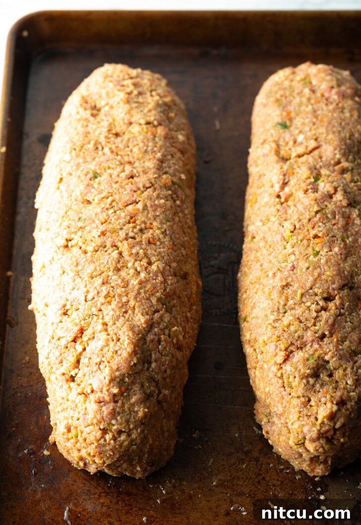 Pitmaster's Meatloaf 9 Two raw, perfectly shaped meatloaves resting side-by-side on a baking sheet, glistening with a coat of barbecue sauce, ready for the smoker.