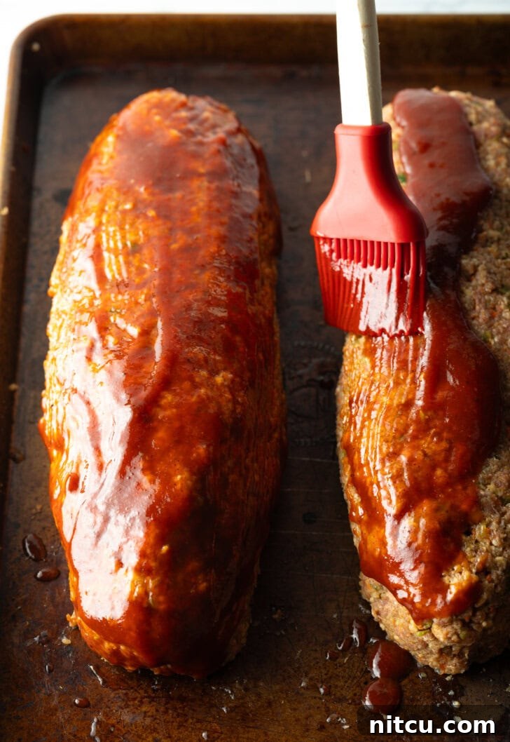 Pitmaster's Meatloaf 10 A close-up view emphasizing the careful application of barbecue sauce to the surface of the raw meatloaf, ensuring a flavorful glaze.