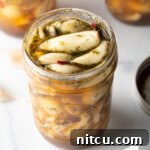 Top down open glass jar stuffed with preserved garlic and herbs.
