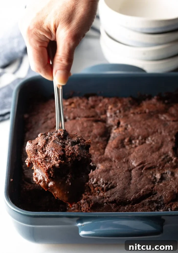 Decadent Chocolate Pudding Cake 2 Hand using a metal spoon to scoop a serving of pudding cake from the baking pan.
