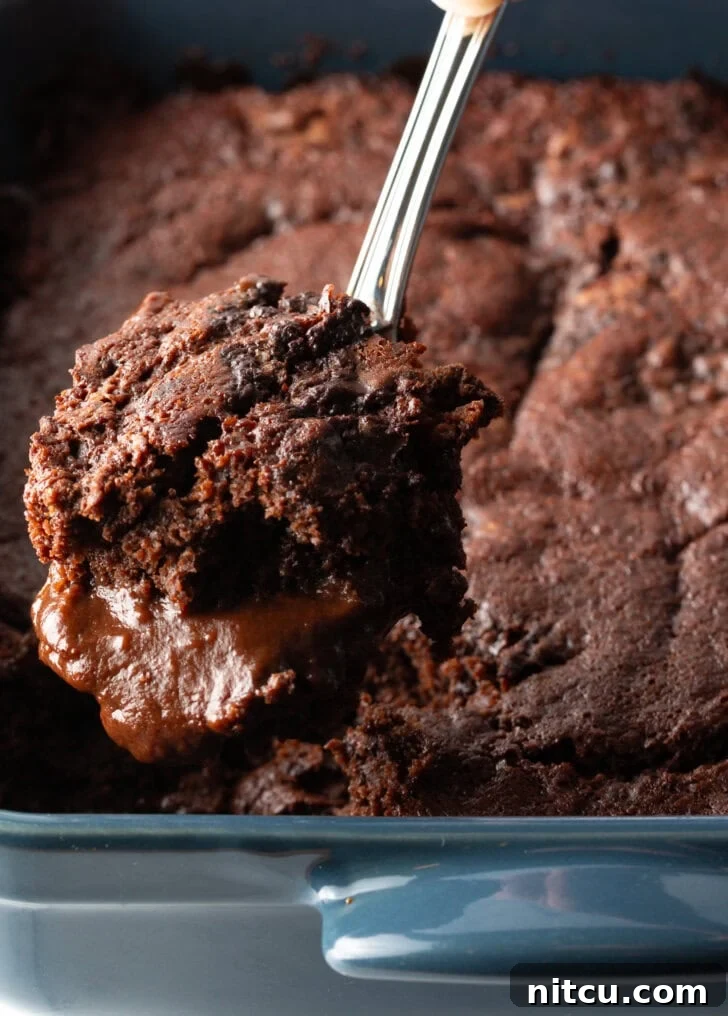 Decadent Chocolate Pudding Cake 10 Hand using a metal spoon to scoop a serving of pudding cake from the baking pan.