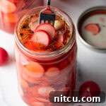 A fork picking out several pickled radishes from a large glass jar, showing the inviting color and crisp texture.