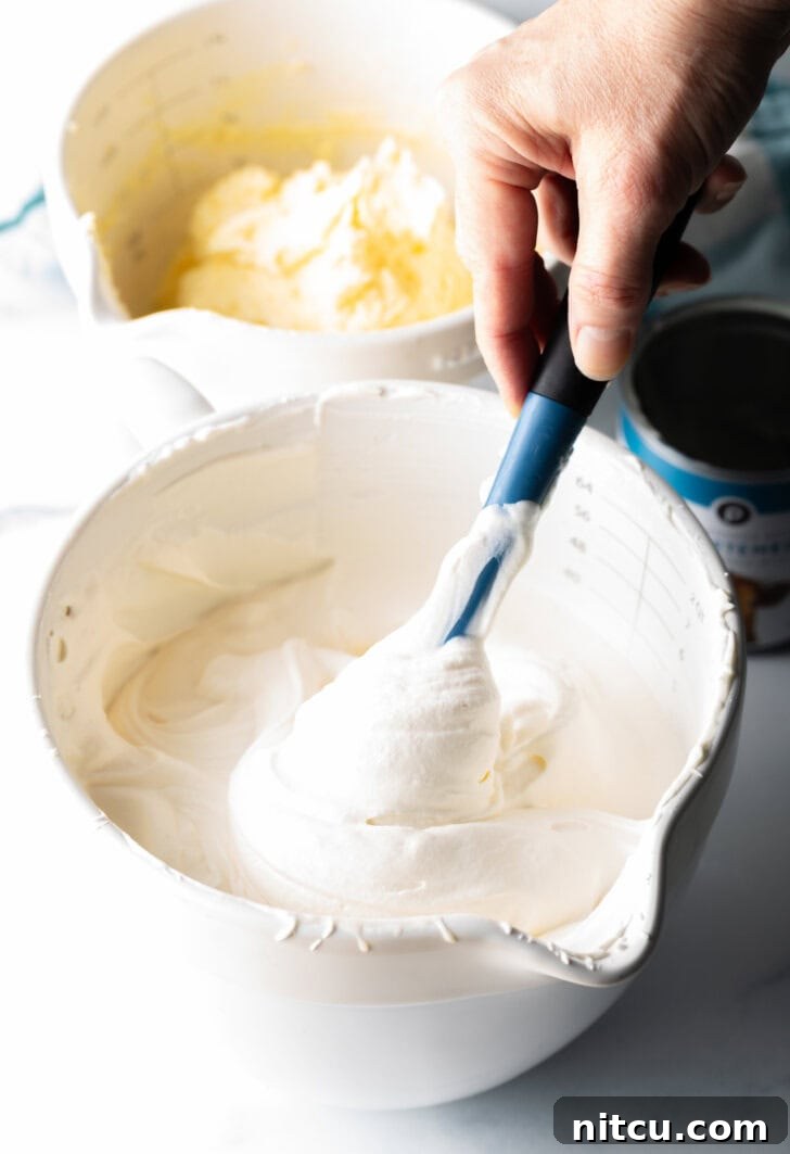 Effortless Banana Pudding Ice Cream 5 A hand gently blending a creamy vanilla ice cream base in a large white mixing bowl using a blue rubber spatula, demonstrating the delicate folding technique.