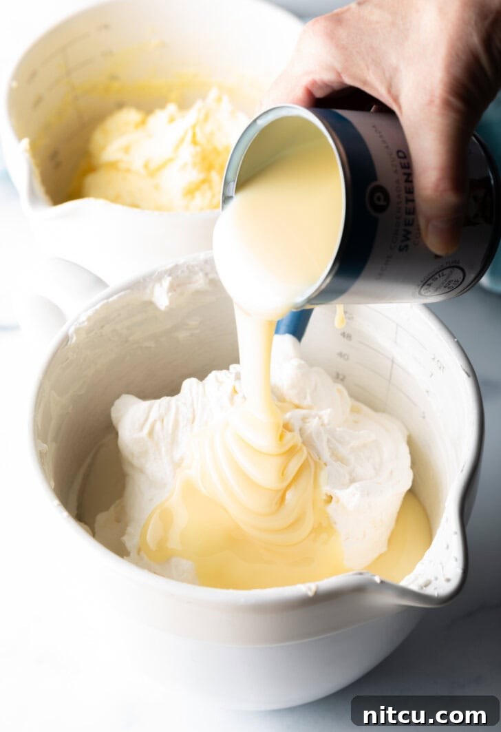Effortless Banana Pudding Ice Cream 6 A hand pouring a stream of luscious sweetened condensed milk over the gently whipped ingredients in a mixing bowl, an essential step for no-churn ice cream.