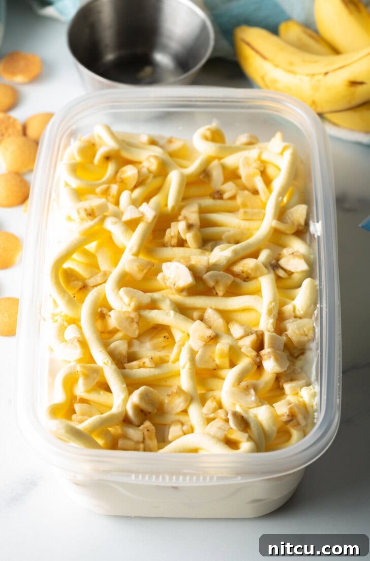 Effortless Banana Pudding Ice Cream 8 Perfectly arranged slices of ripe banana nestled within a rectangular freezer container, layered among the creamy ice cream base, awaiting the next delicious addition.
