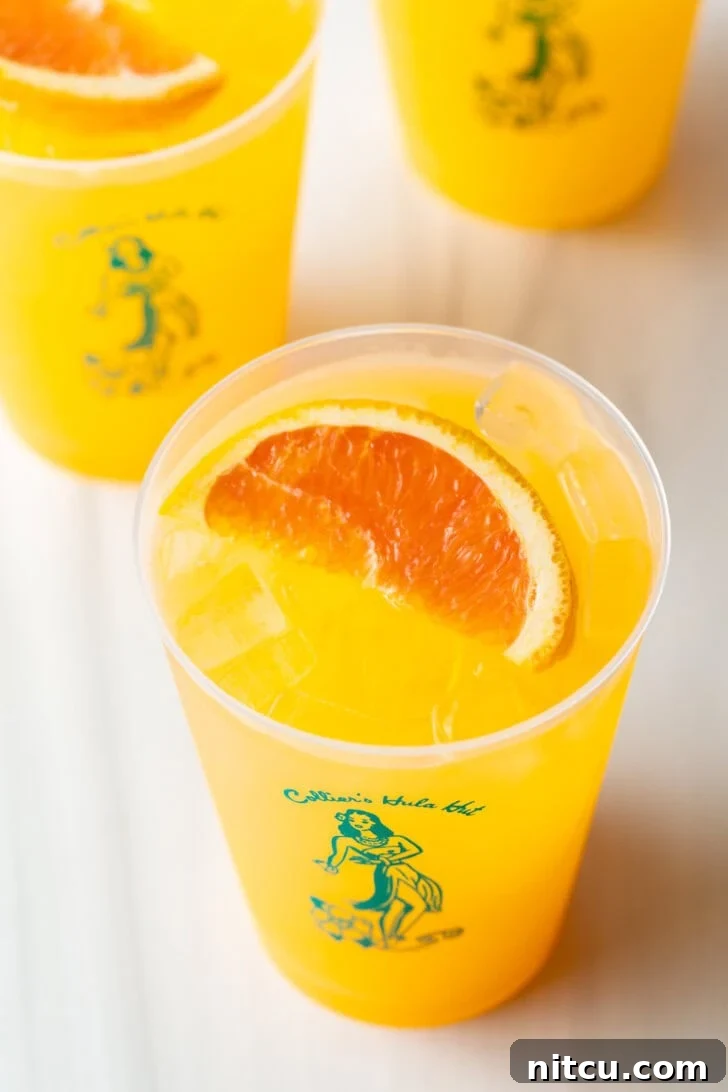 Sunny D Zest Seltzer 3 Top-down view of three Sunny D Vodka Seltzer drinks, each in a glass cup with a slice of orange on top.
