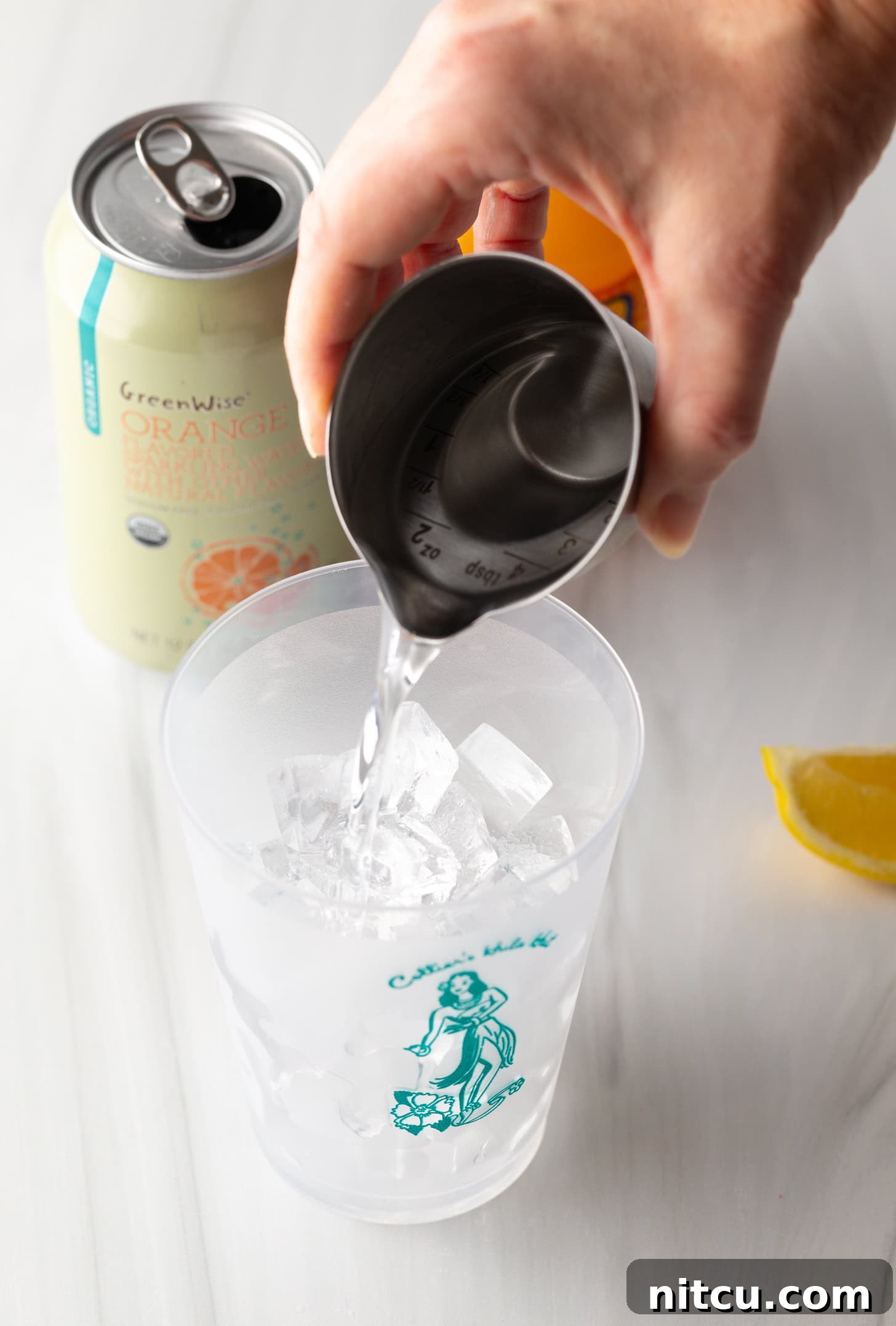 Sunny D Zest Seltzer 5 Hand pouring vodka from a metal shot glass into a glass filled with ice.