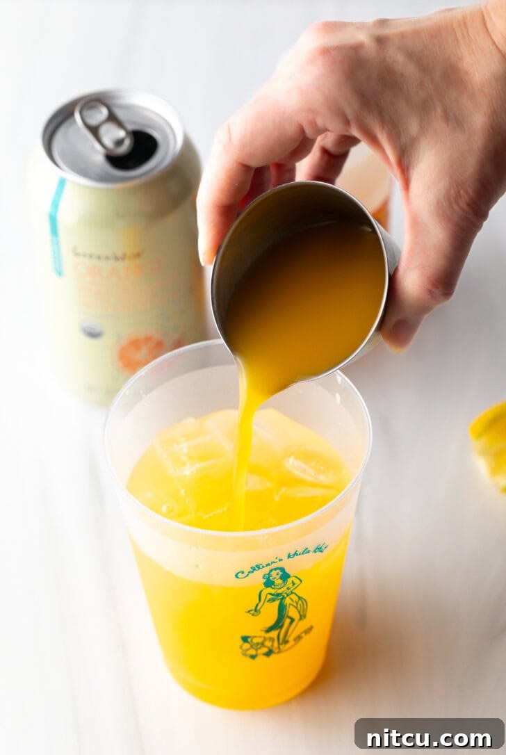 Sunny D Zest Seltzer 7 Hand adding orange juice from a metal shot glass into a glass cup.