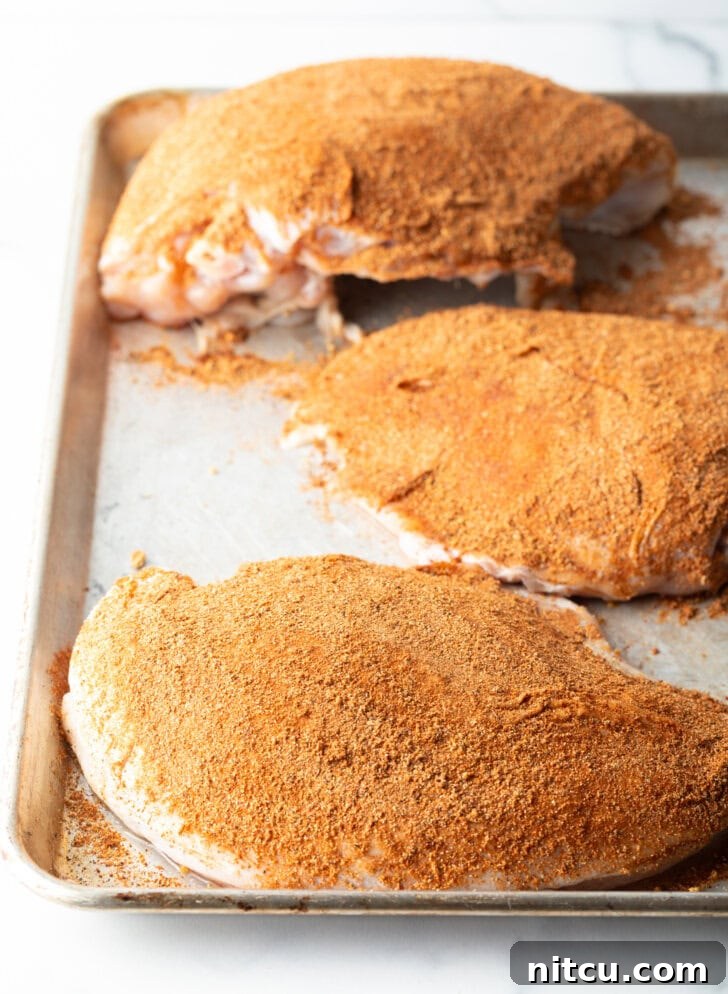 Perfectly Smoked Traeger Turkey Breast 7 Three raw turkey breasts rubbed with seasonings, on a metal baking sheet.