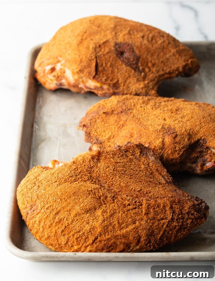 Perfectly Smoked Traeger Turkey Breast 8 Three smoked turkey breasts rubbed with seasonings, on a metal baking sheet.