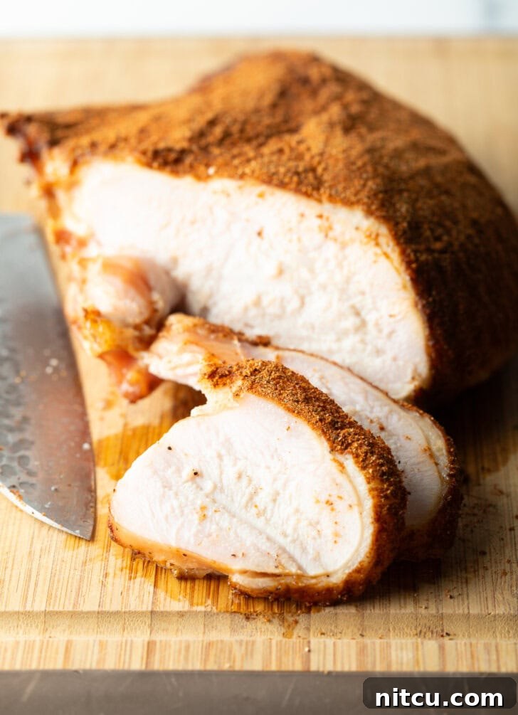 Perfectly Smoked Traeger Turkey Breast 10 Spice-rubbed smoked turkey breast on a wood cutting board, two slices are in front of the breast.