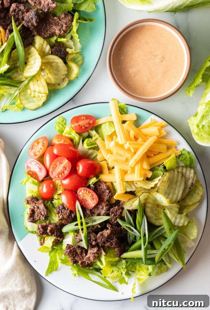 Big Mac Burger Bowl 2 A vibrant, loaded Big Mac cheeseburger salad featuring crisp shredded lettuce, seasoned ground beef crumbles, juicy halved grape tomatoes, rich shredded cheddar cheese, crunchy dill pickles, and fresh sliced green onion, ready for enjoyment.