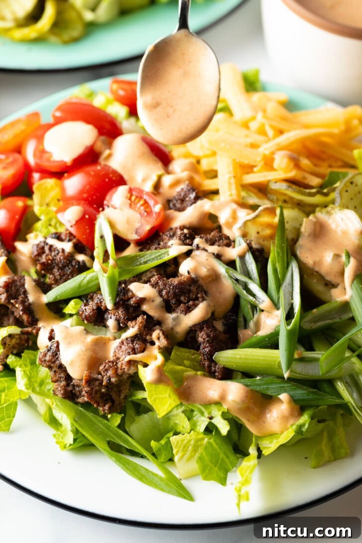 Big Mac Burger Bowl 4 A spoon generously drizzling creamy, golden Big Mac sauce over the loaded burger salad, enhancing its appeal and flavor.