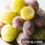 A bowl of green and purple candy grapes. One of the green grapes has been bitten in half to show the inside.