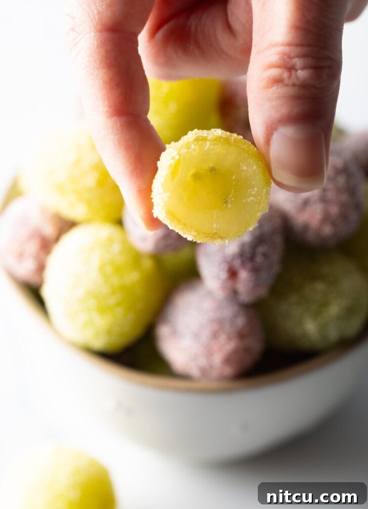 Sweet Grape Gems 10 A bowl of green and purple candy grapes. A hand is holding one of the green grapes to camera. It has been bitten in half to show the inside.
