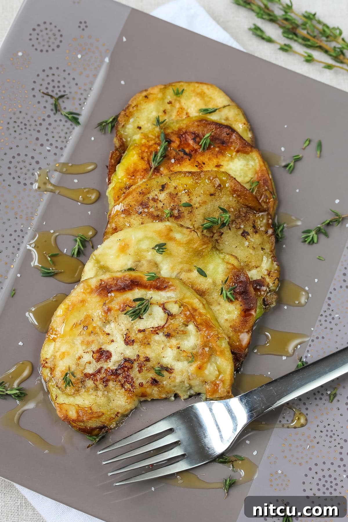 Perfectly Sautéed Eggplant with a golden brown crust, garnished with fresh thyme leaves and a drizzle of golden honey, ready to be served on a rustic plate.