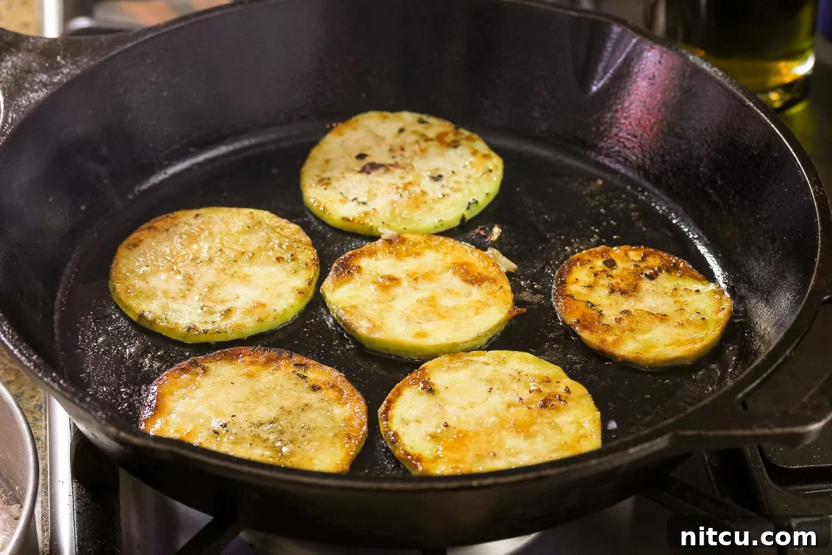 Easy eggplant recipe showing golden brown fried eggplant slices garnished with fresh thyme and a honey drizzle on a white plate, ready for serving.