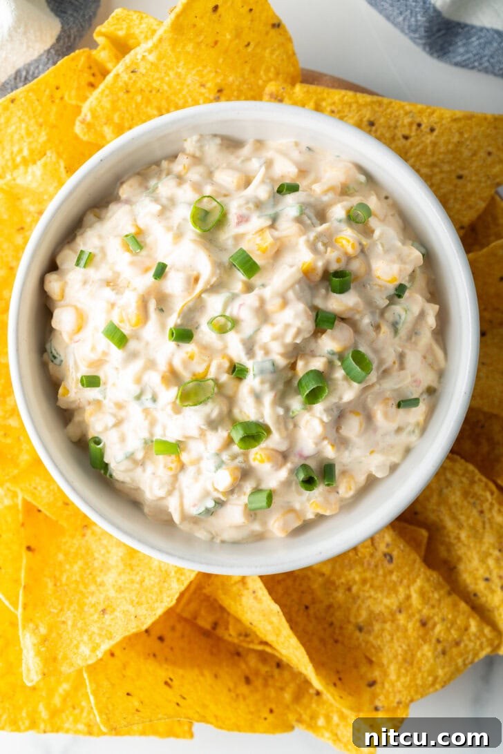 Creamy Street Corn Dip 3 An overhead shot showcasing a vibrant bowl of Mexican street corn dip garnished with fresh green onions, surrounded by crisp tortilla chips, ready for serving.