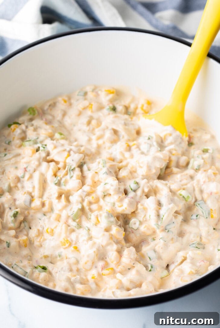 Creamy Street Corn Dip 6 A white bowl of creamy corn dip being gently mixed with a yellow spatula, highlighting the smooth texture.