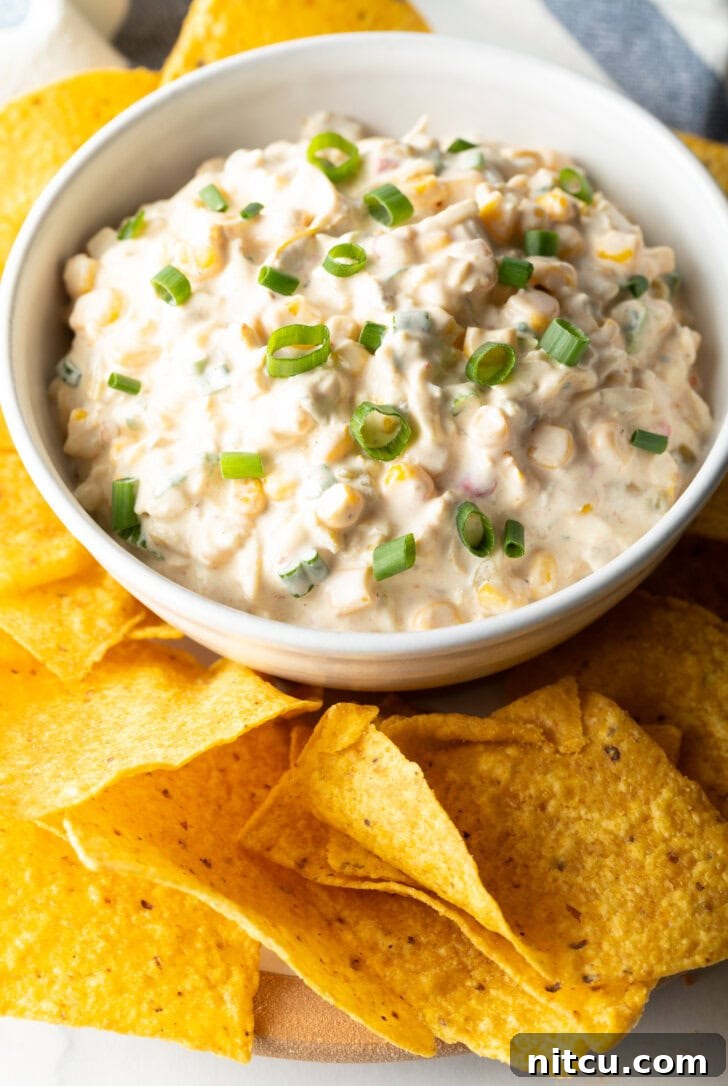 Creamy Street Corn Dip 7 An overhead shot of a white bowl filled with Mexican street corn dip, garnished with sliced green onions, surrounded by golden tortilla chips, invitingly ready to be enjoyed.