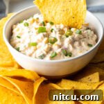Creamy Street Corn Dip 9 Tortilla chip scooping into a white bowl of creamy Mexican corn dip.