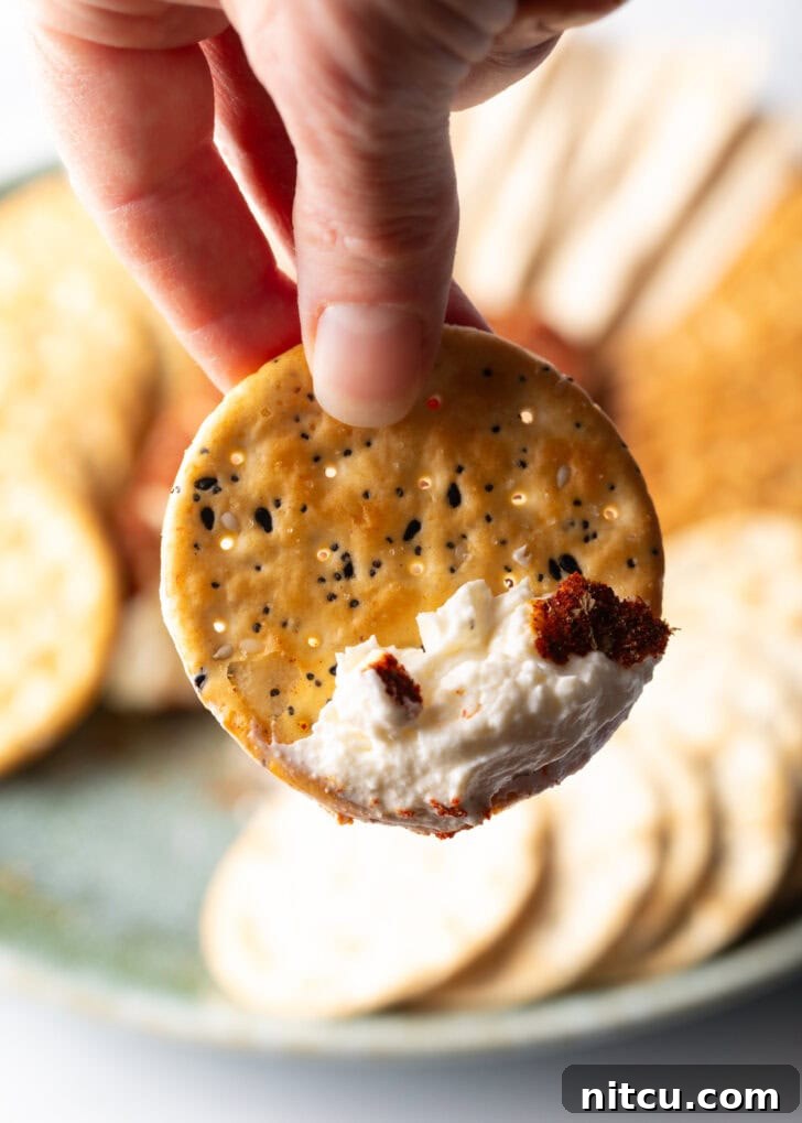 A hand holding a cracker with cream cheese dip to camera.