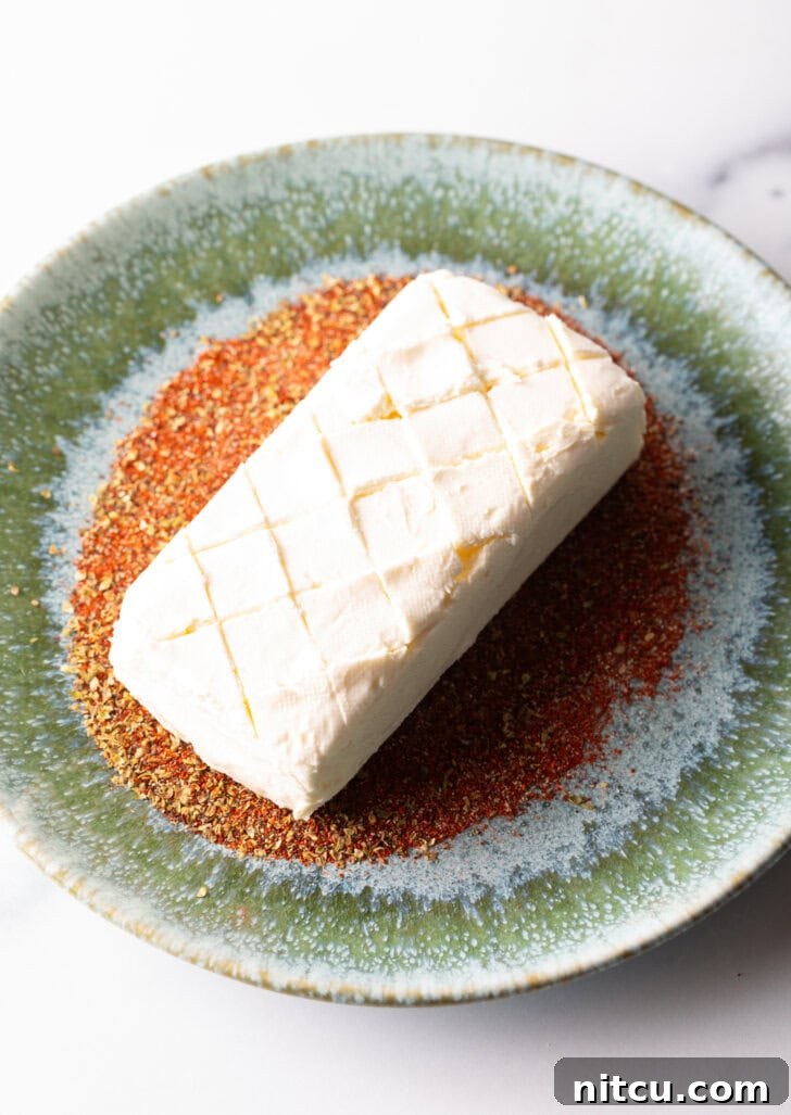 A white block of cream cheese on top of a bed of spices, all on a green plate. The top of the cream cheese has been scoured in a diamond pattern.
