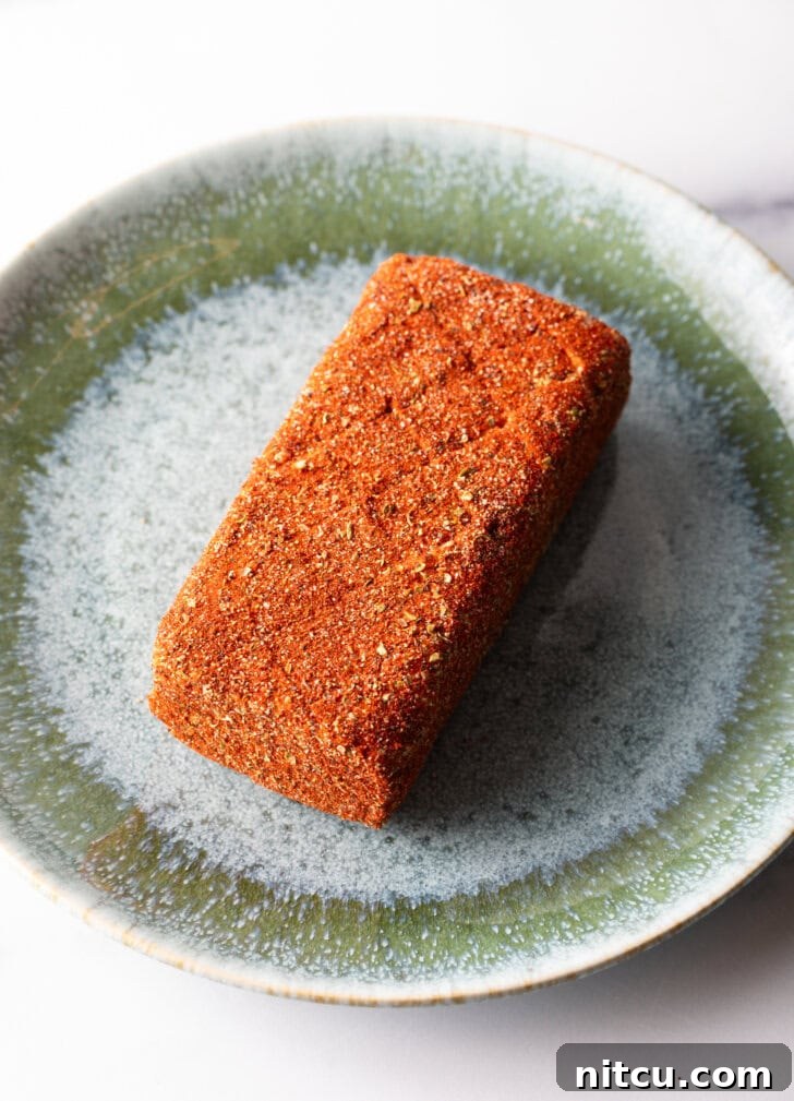 Block of cream cheese coated in spices on a green plate.