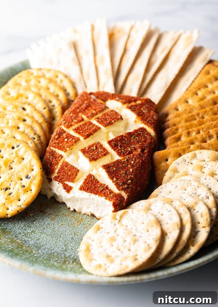 Smoked cream cheese on a green plate surrounded by various types of crackers. A portion of the cheese has been cut away to show the inside.