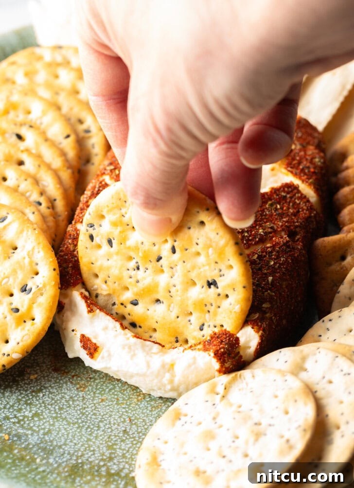 Hand with a cracker scooping a serving of smoked cream cheese from the block, surrounded by crackers.