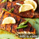 Fiery Blackened Mahi Delight 11 Close view of a fillet of grilled mahi mahi topped with a slice of lemon and green onions. A bite has been removed from the fish to show the white flaky inside of the meat.