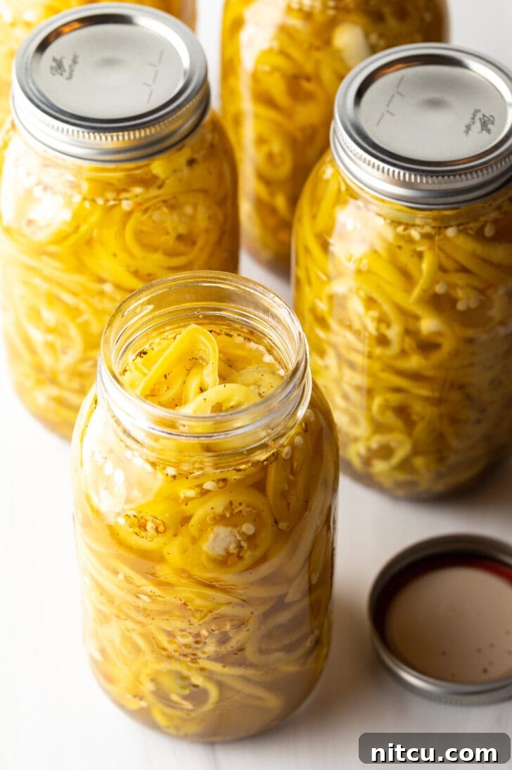 Sweet and Tangy Pickled Banana Peppers 2 4 large jars of canned pickled banana peppers. The jar closest to the camera has the lid off showing the slices of peppers filling the jar.