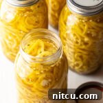Sweet and Tangy Pickled Banana Peppers 12 Four jars of homemade pickled banana peppers, with one open jar showing sliced peppers.