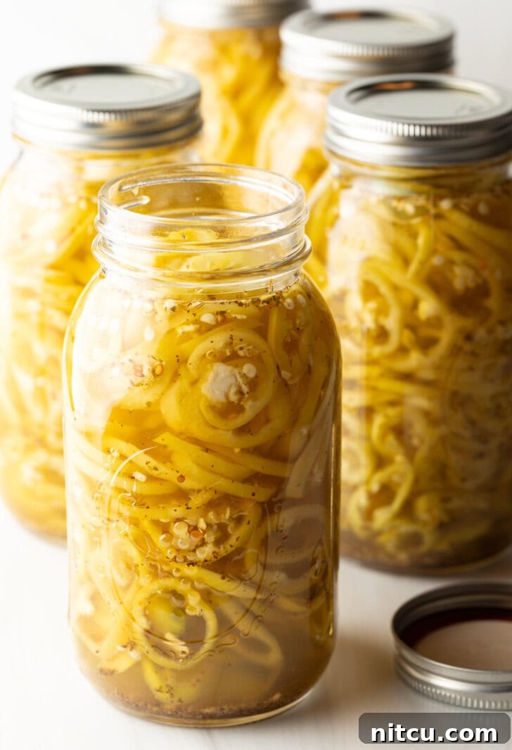 Sweet and Tangy Pickled Banana Peppers 10 4 large jars of canned pickled banana peppers. The jar closest to the camera has the lid off showing the slices of peppers filling the jar.