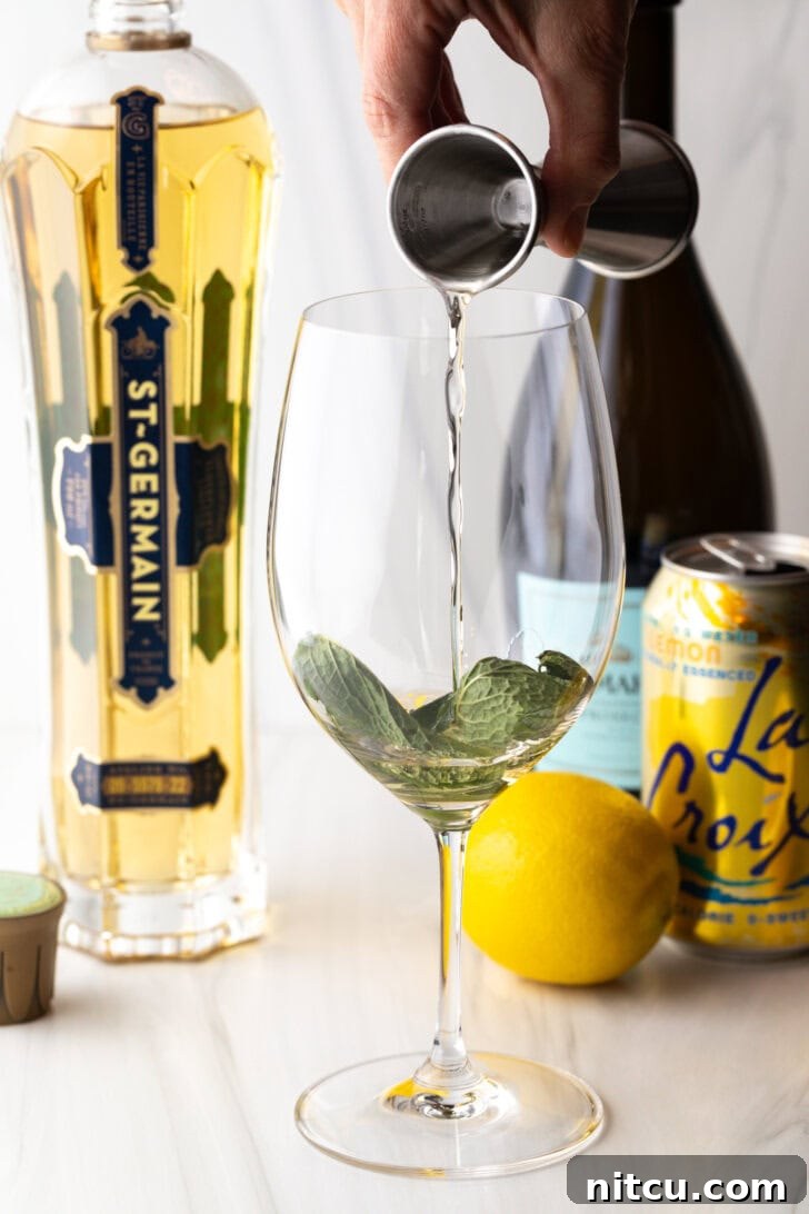 St-Germain Garden Spritz 4 Hand adding liquor from a metal shot glass on top of the muddled mint leaves.
