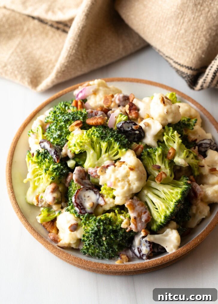 Vibrant Broccoli Cauliflower Salad 2 Bowl of crisp broccoli and cauliflower salad, beautifully tossed with crunchy pecans, vibrant red onions, and sweet dried cranberries, ready to be served.