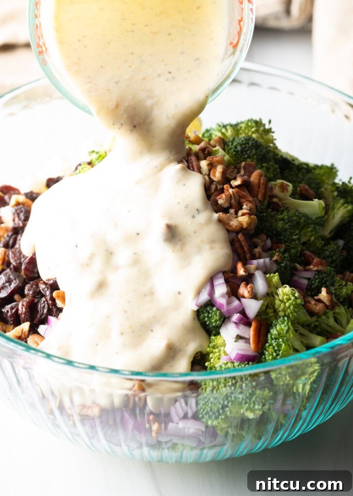 Vibrant Broccoli Cauliflower Salad 7 Creamy mayonnaise-based dressing being poured from a glass measuring cup onto the vibrant salad ingredients in a large glass bowl, illustrating the final step before tossing.